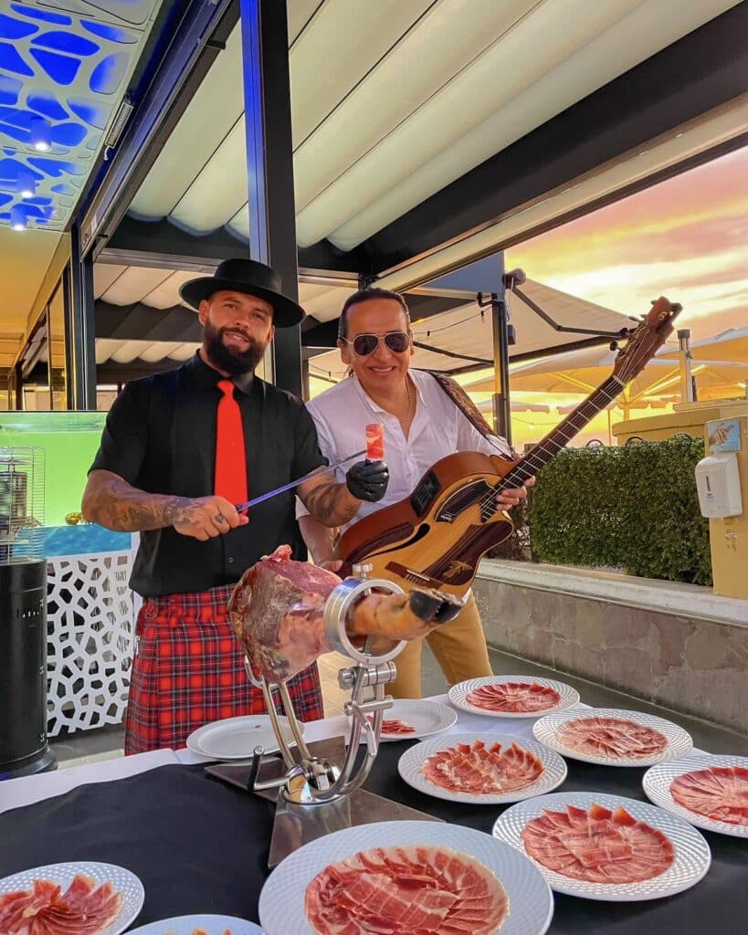 Julio García de Galician Ham Carver sirviendo jamón ibérico en evento en Tenerife junto a músico en directo.