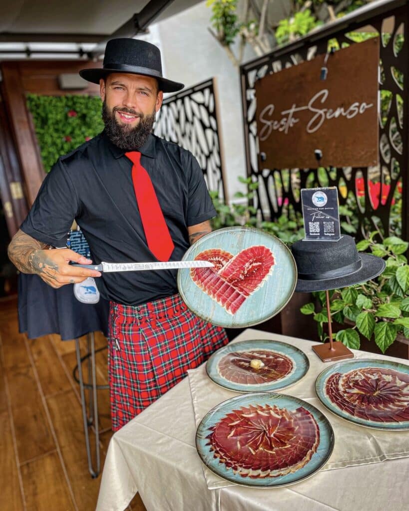 Julio García, maestro cortador de Galician Ham Carver, presentando una bandeja de jamón ibérico en forma de corazón en un evento en Playa San Juan, Tenerife.