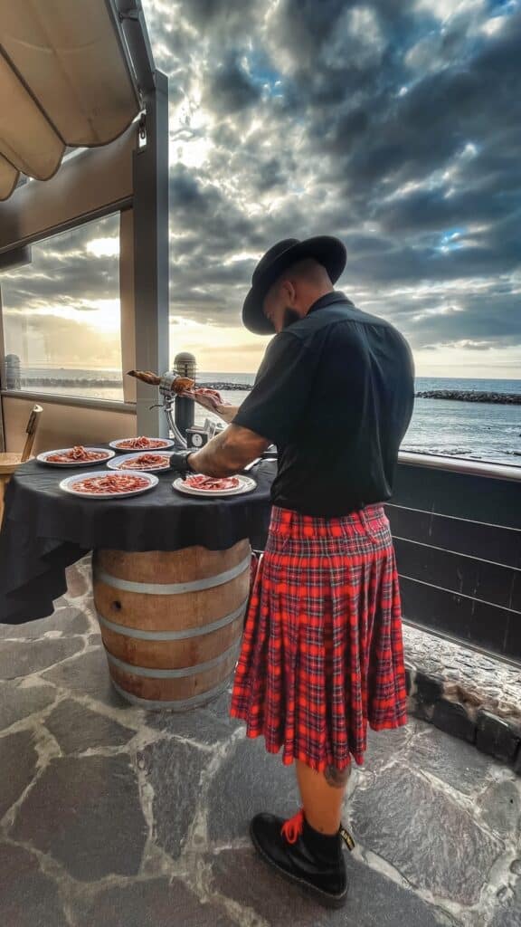 Julio García, cortador de jamón de Galician Ham Carver, preparando platos de jamón ibérico al atardecer en Playa del Bobo, Tenerife sur, durante un aniversario frente al mar.