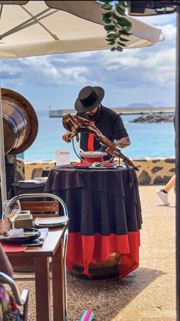 Cortador de jamón Julio García, Galician Ham Carver, ofreciendo espectáculo gastronómico en evento frente al mar.