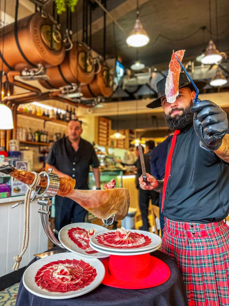 Cortador de jamón de Galician Ham Carver realizando un corte artesanal de jamón ibérico en vivo durante una colaboración en una taberna tradicional del centro histórico, ofreciendo una experiencia gastronómica única