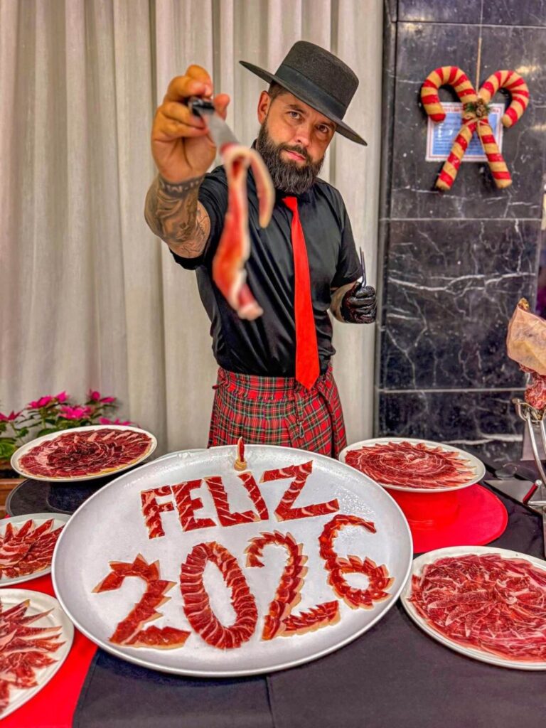 Show de corte artístico de jamón en gala de fin de año 2025 – Galician Ham Carver Santa Cruz de Tenerife Julio García, Galician Ham Carver, durante la gala de fin de año en la Residencia Militar Paso Alto, Santa Cruz de Tenerife, mostrando una loncha de jamón junto a un plato artístico con el mensaje Feliz 2026